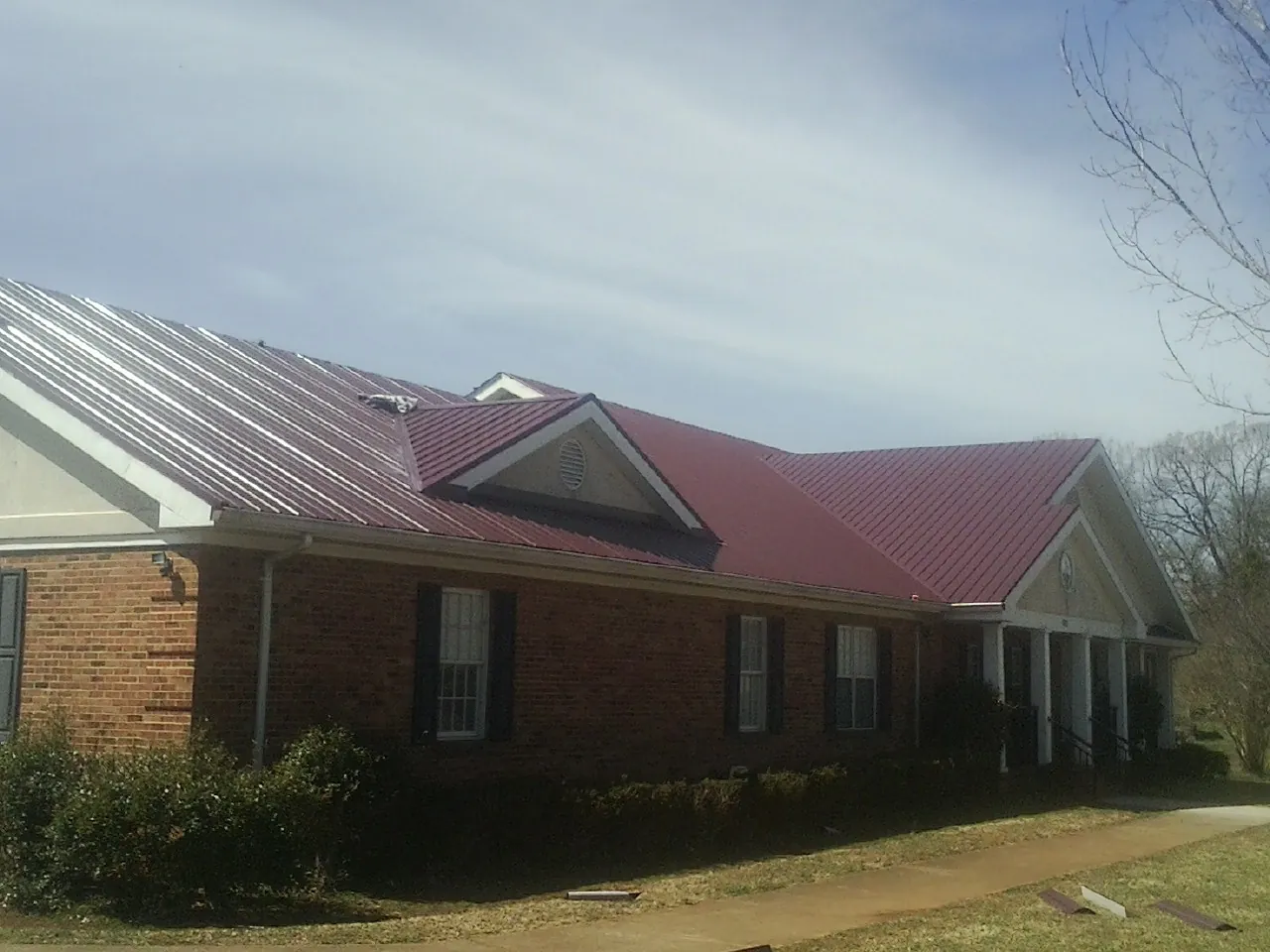 Red metal roof with gabled entries on a long brick building, from a Hail Damage Roof Repair job in Carver