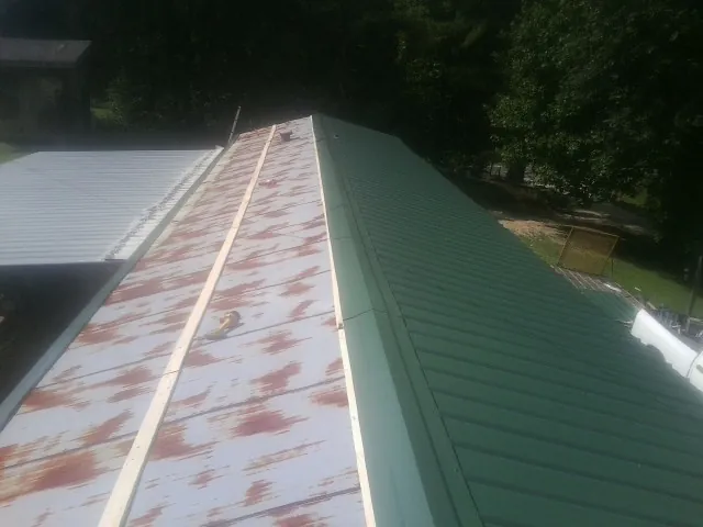 Old rusted panels beside newly installed green metal roofing — Wind Damage Roof Repair by Roofing Brothers in Carver
