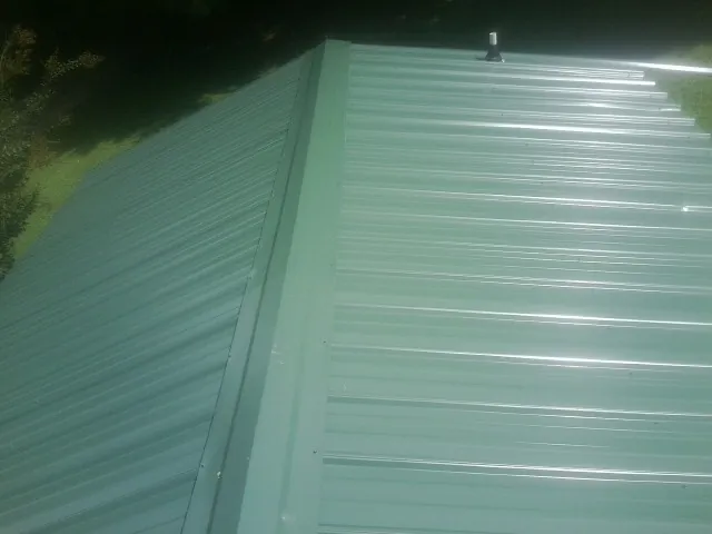 New green metal panels meeting at the ridge of a roof — Flat Roof Repair work by our crew in Carver