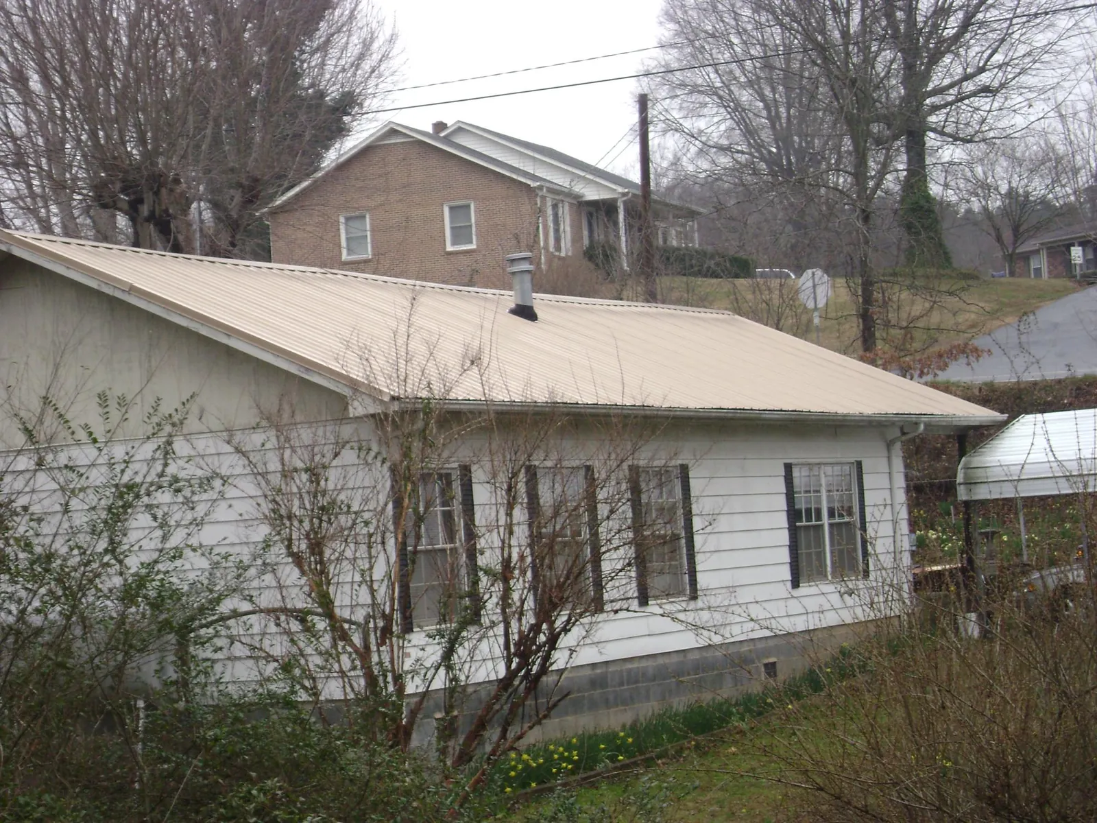Tan metal roof on a white sided house set into a hillside — Commercial Roofing by Roofing Brothers in Carver