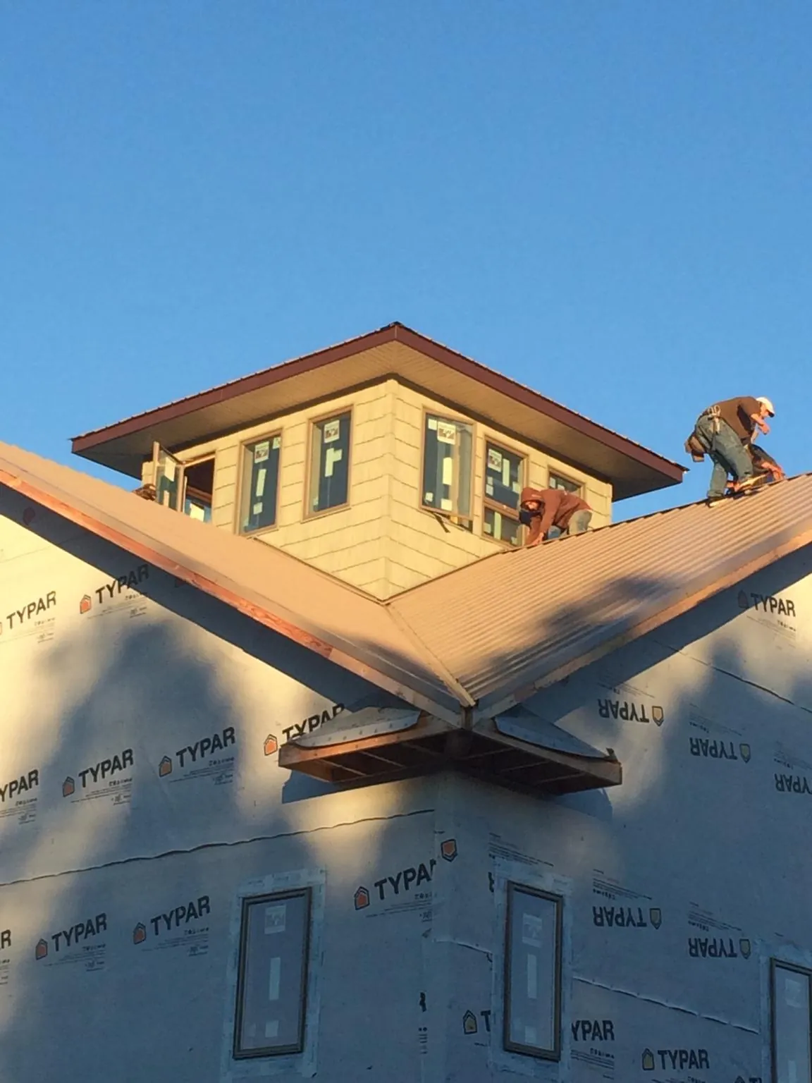 Roofers working around a rooftop cupola on a new metal roof at sunset — Roof Waterproofing in Carver by Roofing Brothers